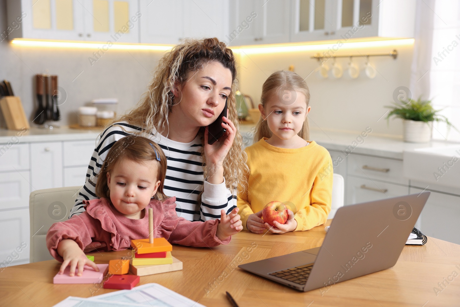 Photo of Single mother talking on smartphone and her daughters at table in kitchen