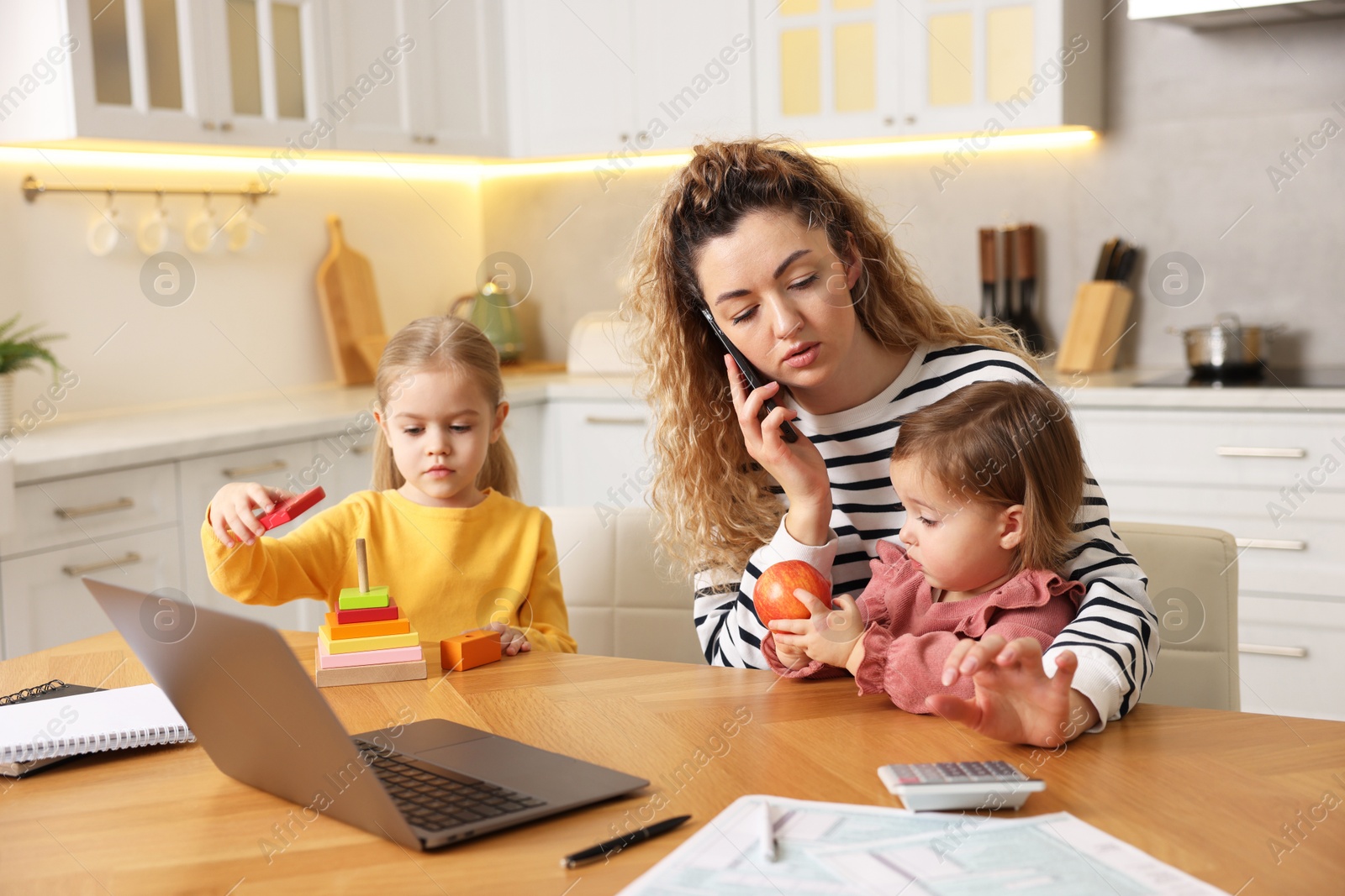 Photo of Single mother talking on smartphone and her daughters at table in kitchen