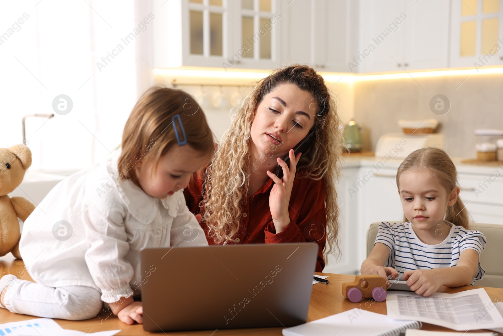 Photo of Work-family balance. Single mother talking on smartphone and her daughters at table in kitchen