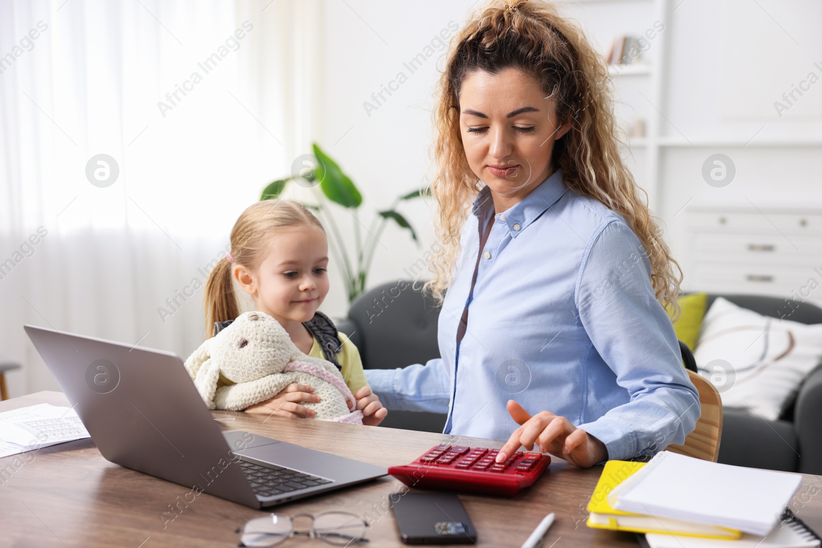 Photo of Work-family balance. Single mother using calculator and her daughter at table indoors