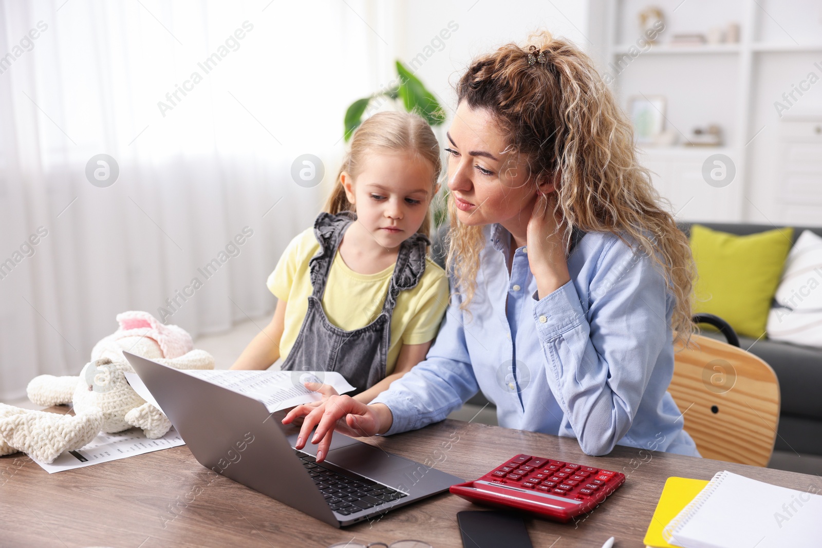 Photo of Single mother working on laptop and her daughter at table indoors