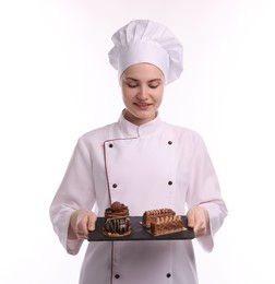 Photo of Happy confectioner in uniform holding delicious chocolate desserts on white background