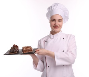 Photo of Happy confectioner in uniform holding delicious chocolate desserts on white background