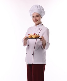 Photo of Happy confectioner in uniform holding delicious profiteroles with strawberries on white background