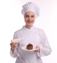 Photo of Happy confectioner in uniform holding delicious chocolate dessert and bottle of sauce on white background