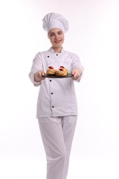 Photo of Happy confectioner in uniform holding delicious profiteroles with strawberries on white background