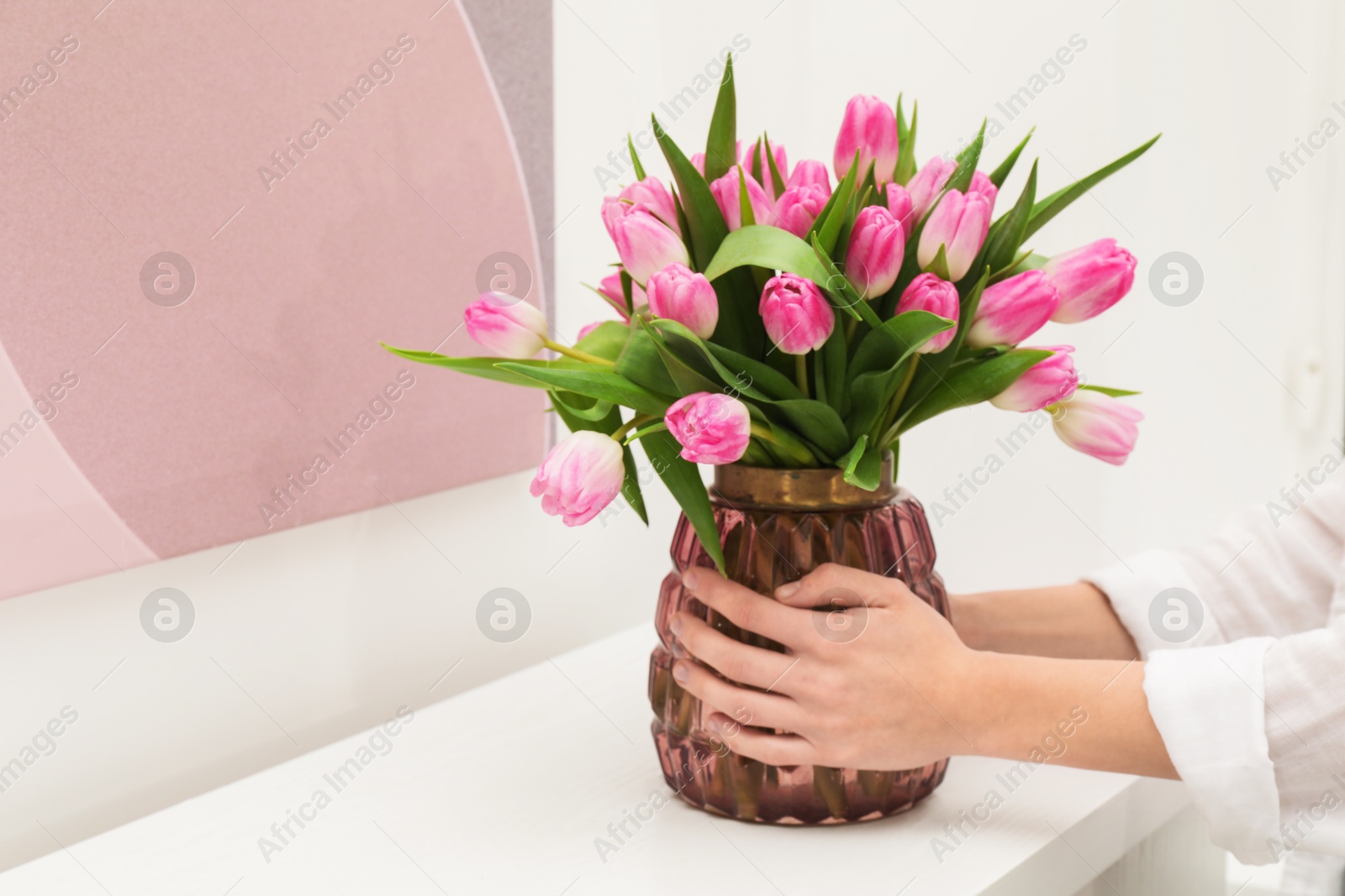 Photo of Woman arranging vase with bouquet of beautiful tulips onto window sill indoors, closeup. Space for text