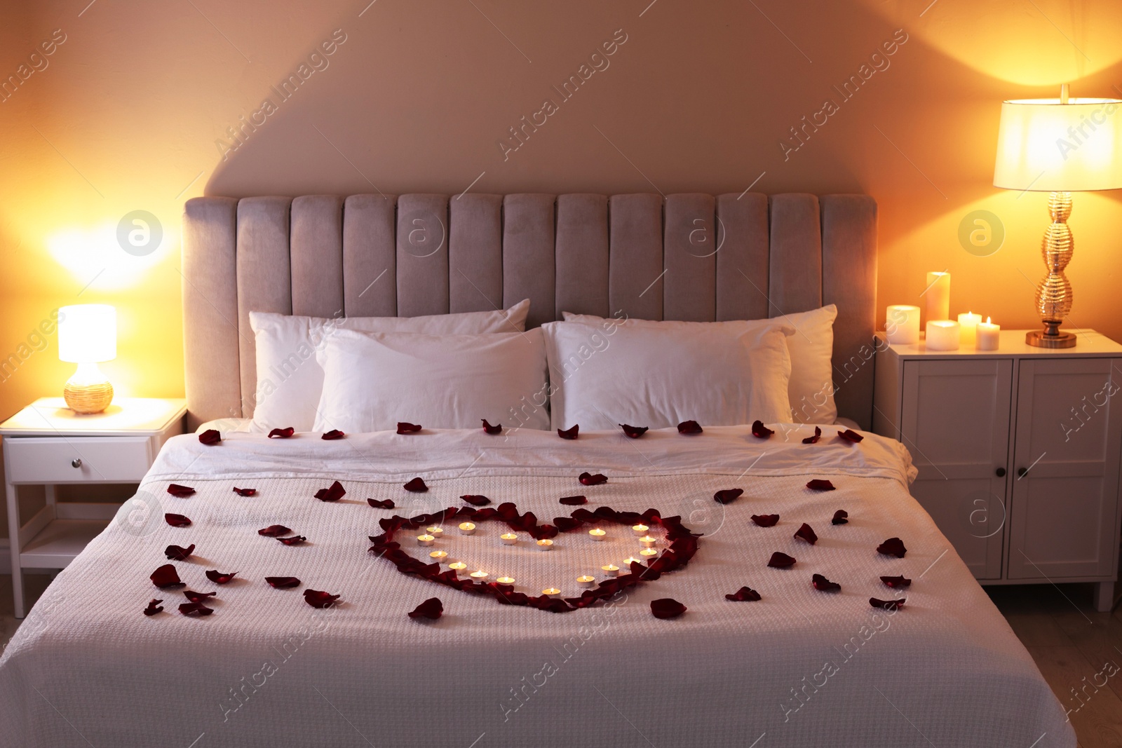 Heart made with beautiful rose petals and burning candles on bed indoors Photo of Heart made with beautiful rose petals and burning candles on bed indoors