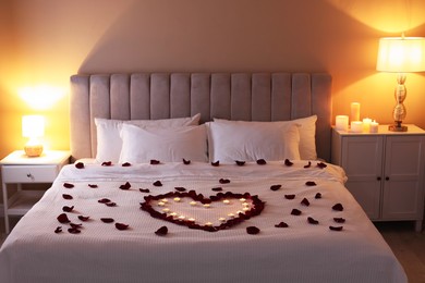 Photo of Heart made with beautiful rose petals and burning candles on bed indoors