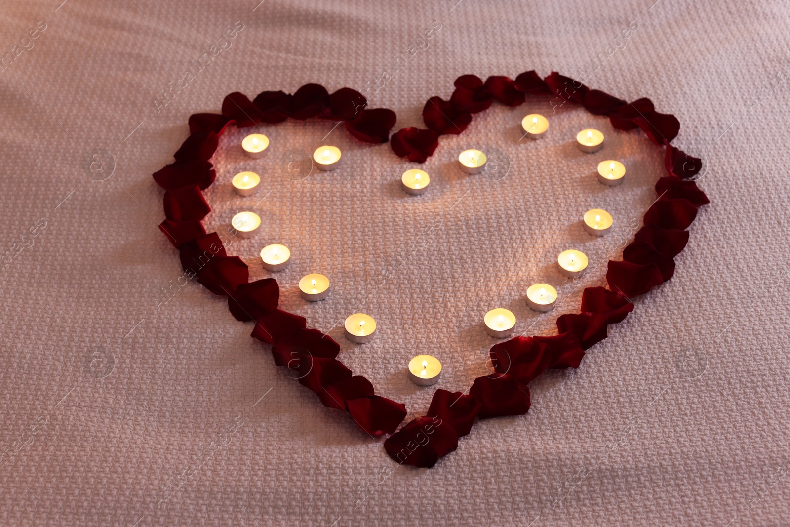 Heart made with beautiful rose petals and burning candles on bed Photo of Heart made with beautiful rose petals and burning candles on bed