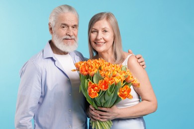 Photo of Happy couple with bouquet of tulips on light blue background