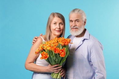 Photo of Cute couple with bouquet of tulips on light blue background