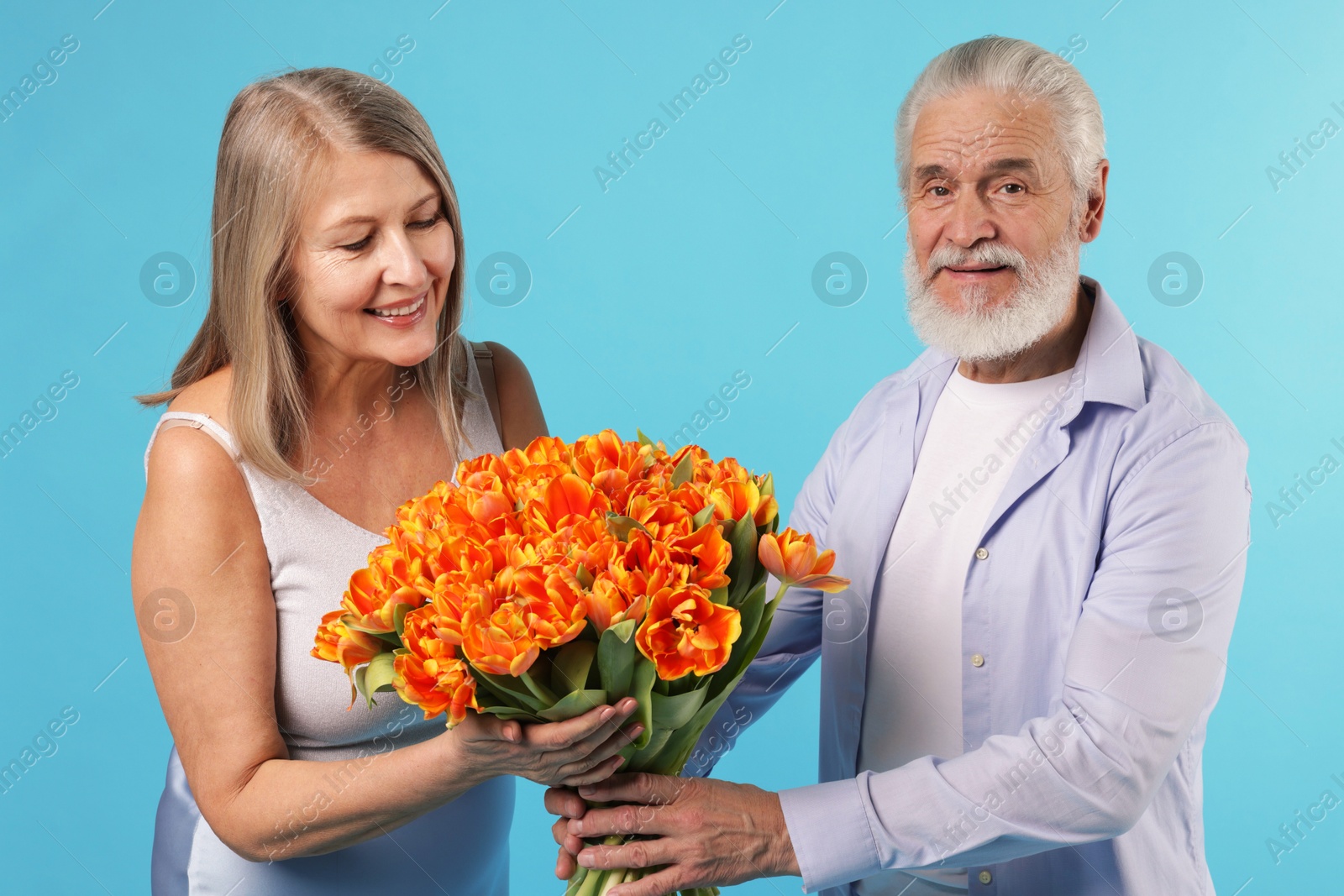 Photo of Man presenting bouquet of tulips to his happy wife on light blue background