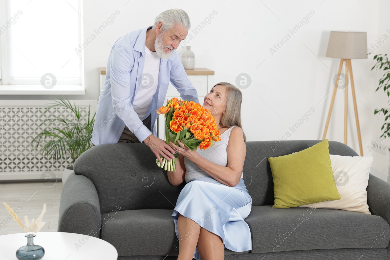 Photo of Man presenting bouquet of tulips to his happy wife at home