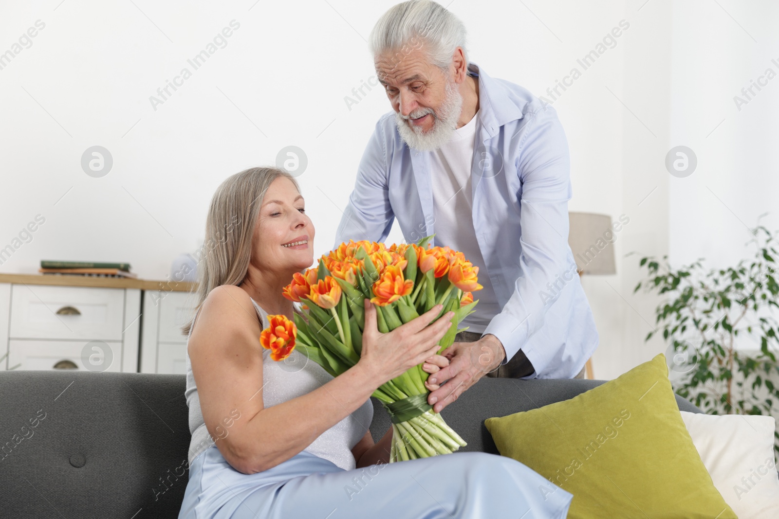 Photo of Man presenting bouquet of tulips to his happy wife at home