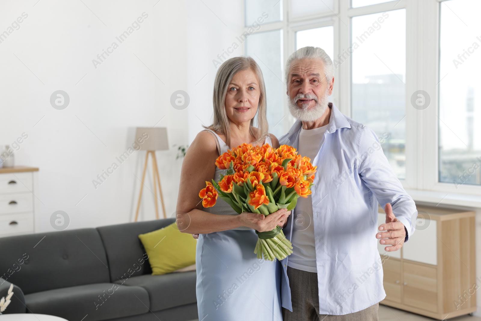 Photo of Cute couple with bouquet of tulips at home. Space for text