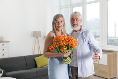 Photo of Cute couple with bouquet of tulips at home. Space for text