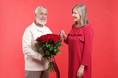 Photo of Man presenting bouquet of roses to his happy wife on red background