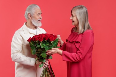 Photo of Man presenting bouquet of roses to his happy wife on red background