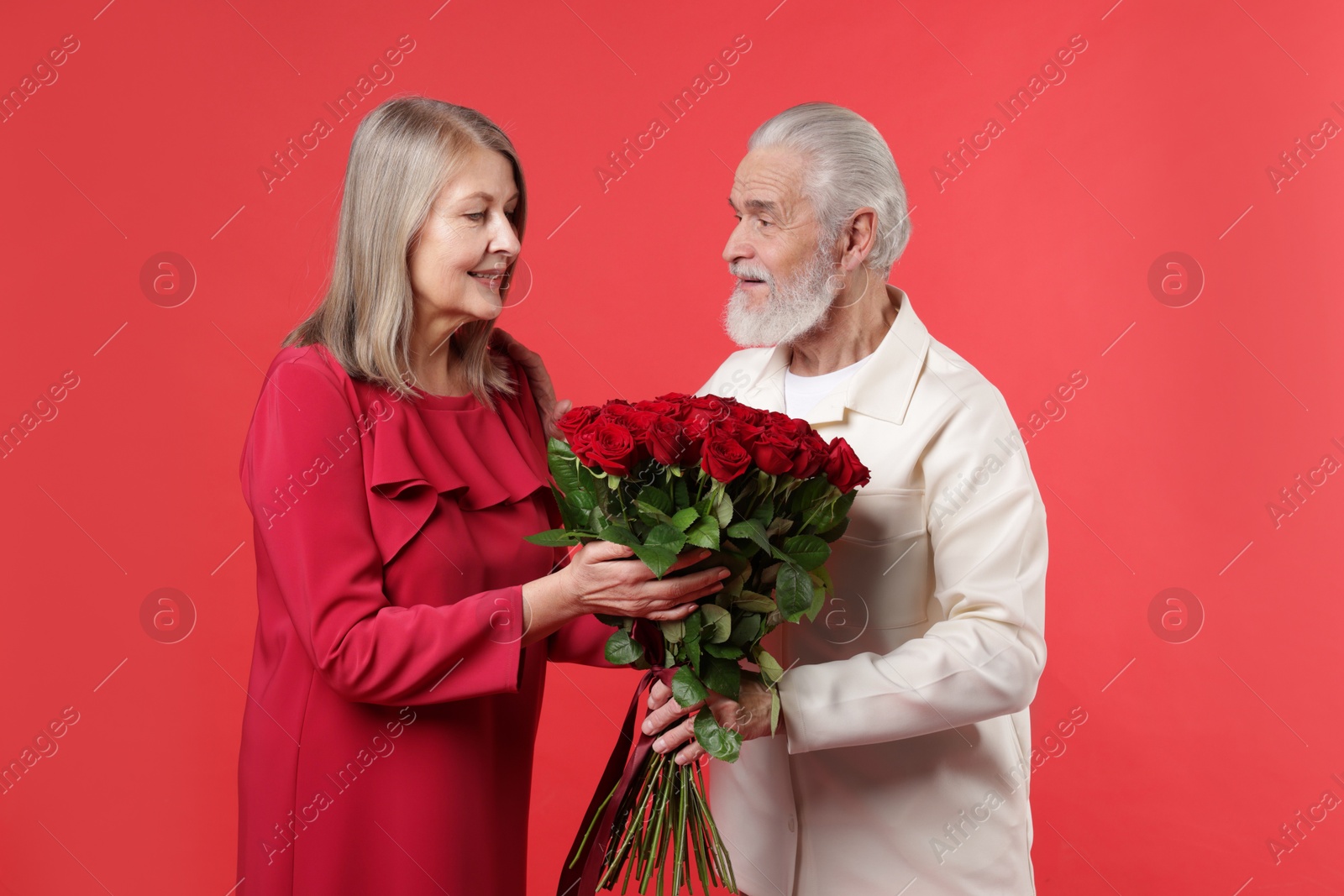 Photo of Man presenting bouquet of roses to his happy wife on red background