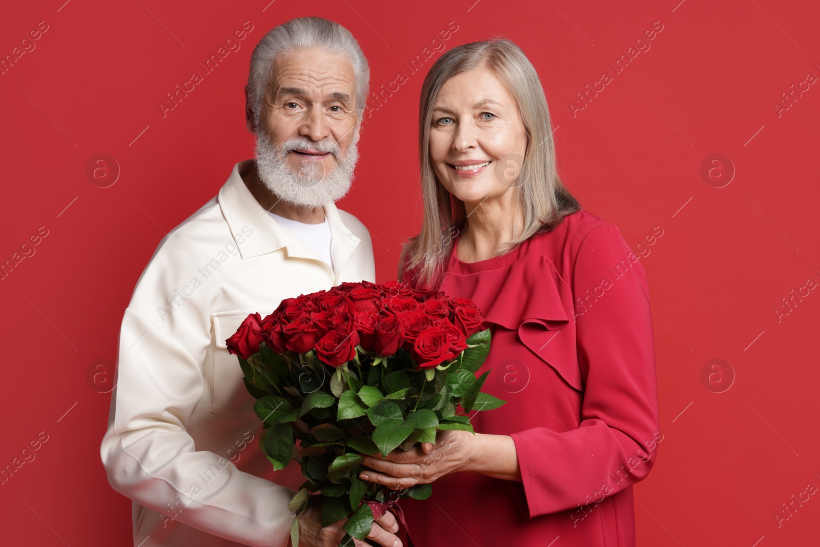 Photo of Happy couple with bouquet of roses on red background