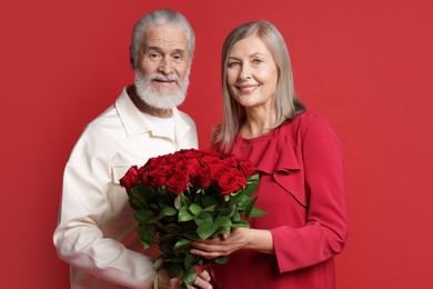 Photo of Happy couple with bouquet of roses on red background