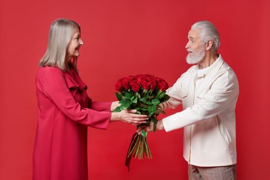 Photo of Man presenting bouquet of roses to his happy wife on red background