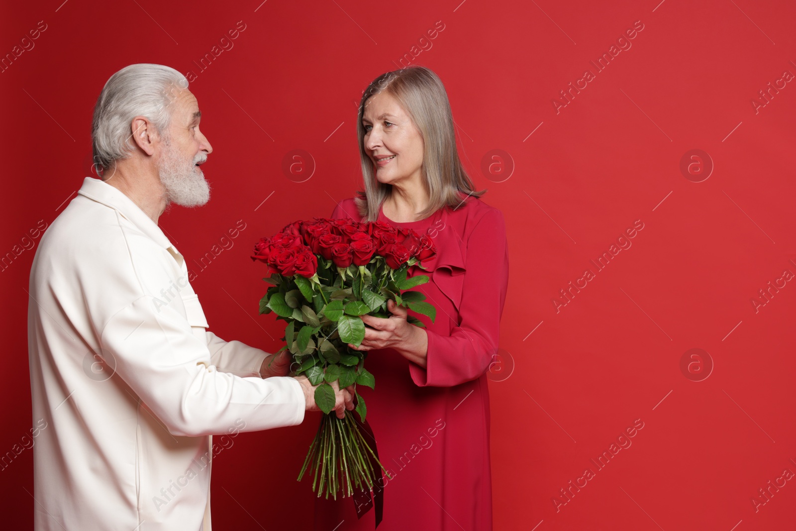 Photo of Man presenting bouquet of roses to his happy wife on red background. Space for text