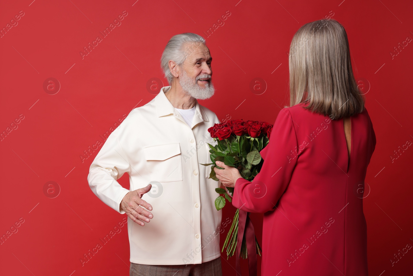 Photo of Man presenting bouquet of roses to his wife on red background