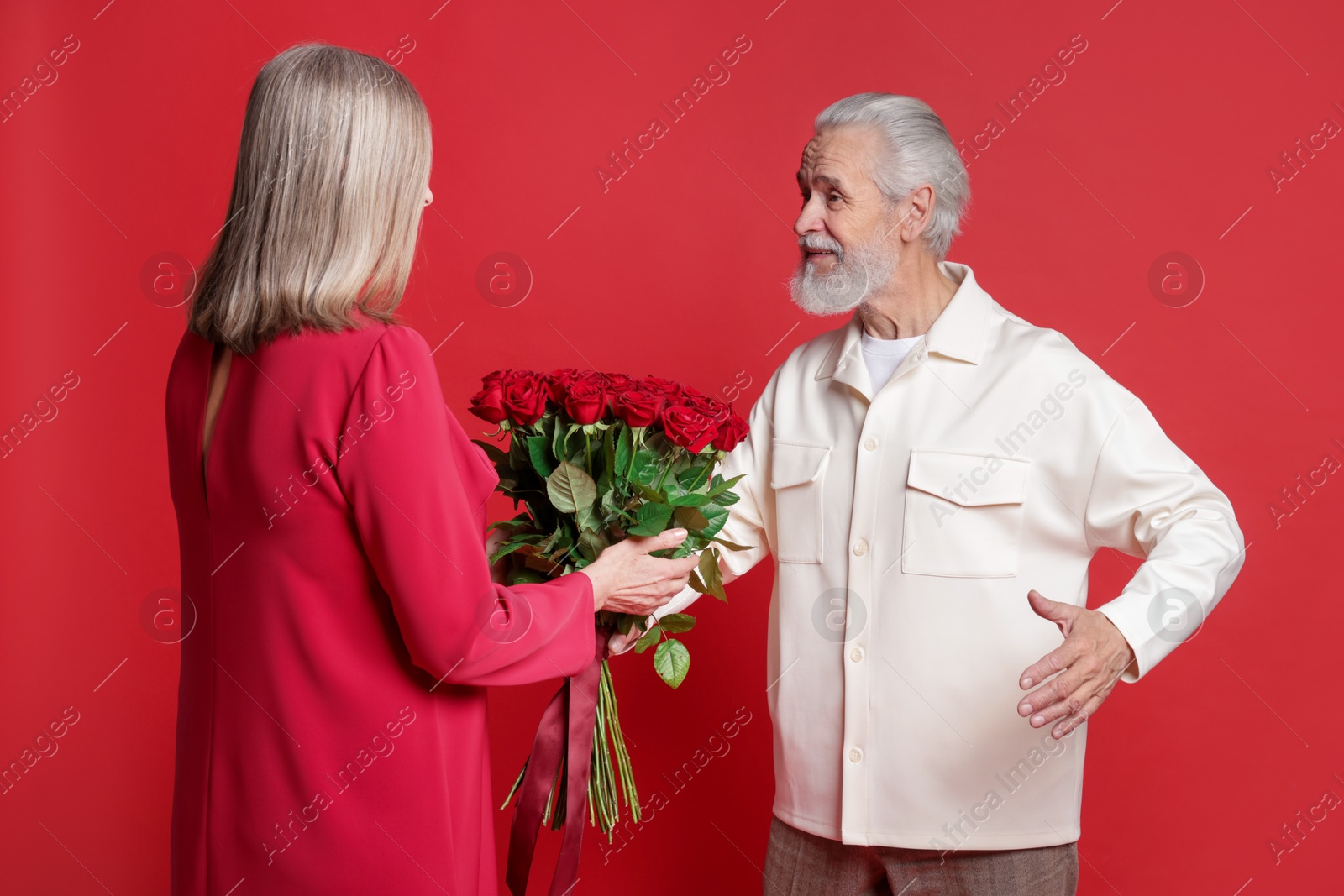 Photo of Man presenting bouquet of roses to his wife on red background