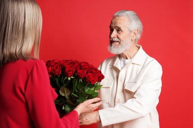 Photo of Man presenting bouquet of roses to his wife on red background