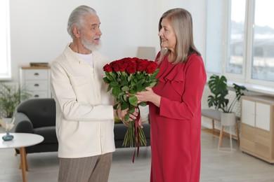 Photo of Happy couple with bouquet of red roses at home