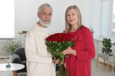 Photo of Happy couple with bouquet of red roses at home