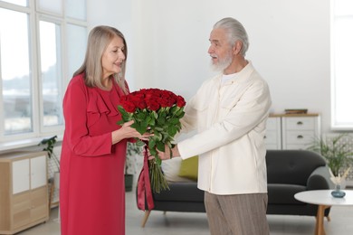 Photo of Man presenting bouquet of roses to his happy wife at home