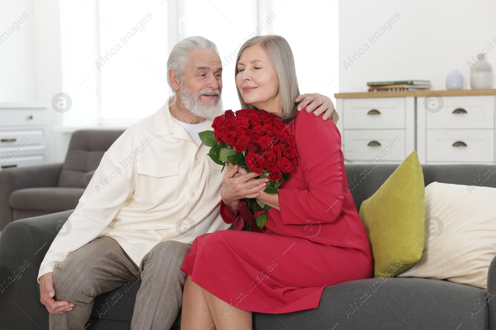 Photo of Happy couple with bouquet of red roses on sofa at home