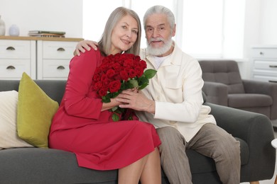 Photo of Happy couple with bouquet of red roses on sofa at home