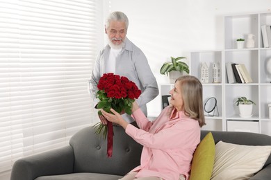 Photo of Man presenting bouquet of roses to his happy wife at home