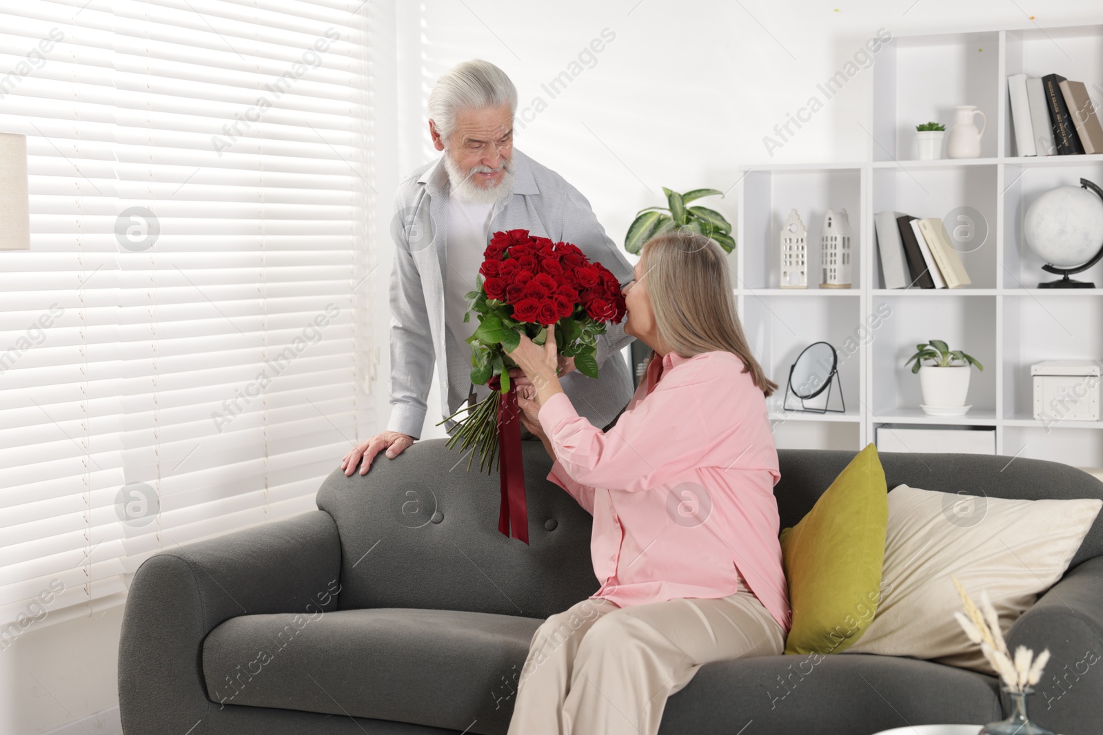 Photo of Man presenting bouquet of roses to his wife at home