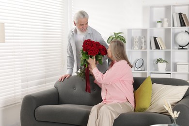 Photo of Man presenting bouquet of roses to his wife at home