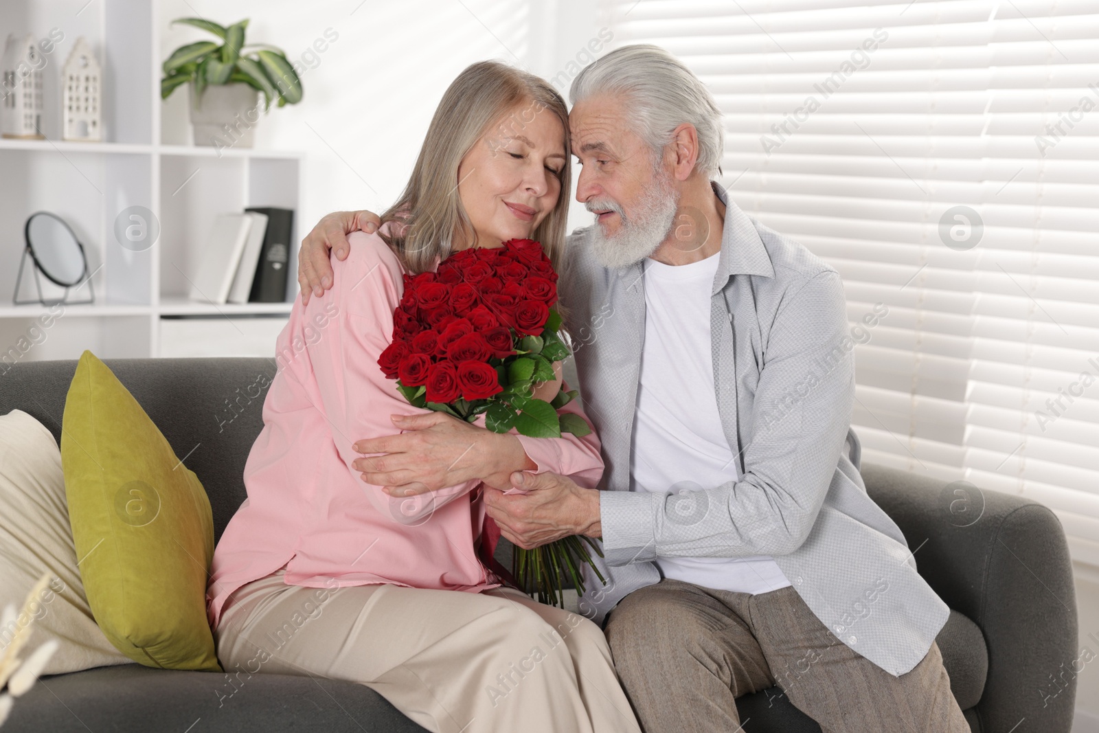 Photo of Happy couple with bouquet of red roses on sofa at home