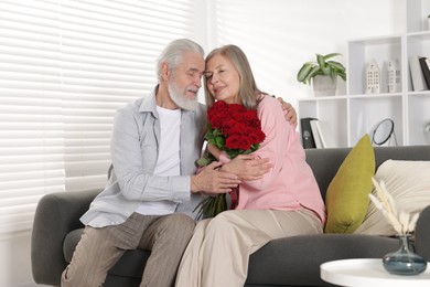 Photo of Happy couple with bouquet of red roses on sofa at home