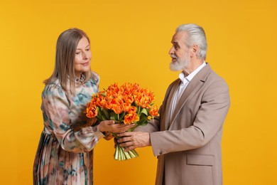 Photo of Man presenting bouquet of tulips to his wife on yellow background