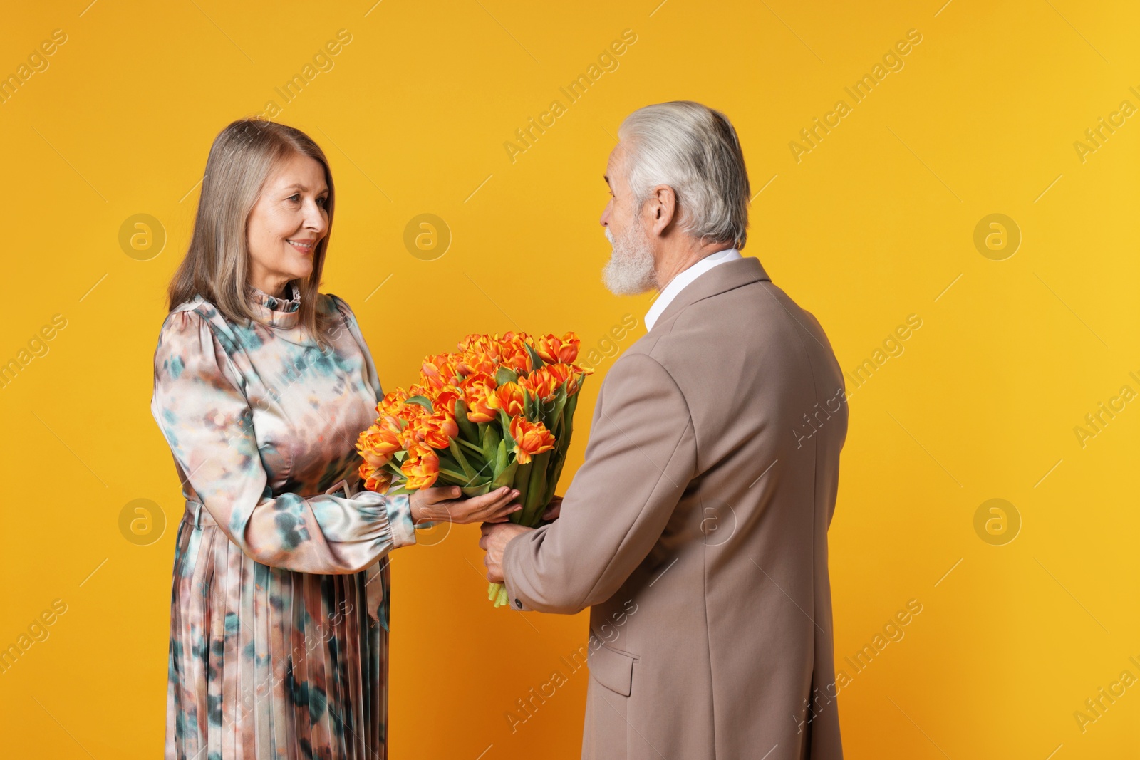 Photo of Man presenting bouquet of tulips to his happy wife on yellow background