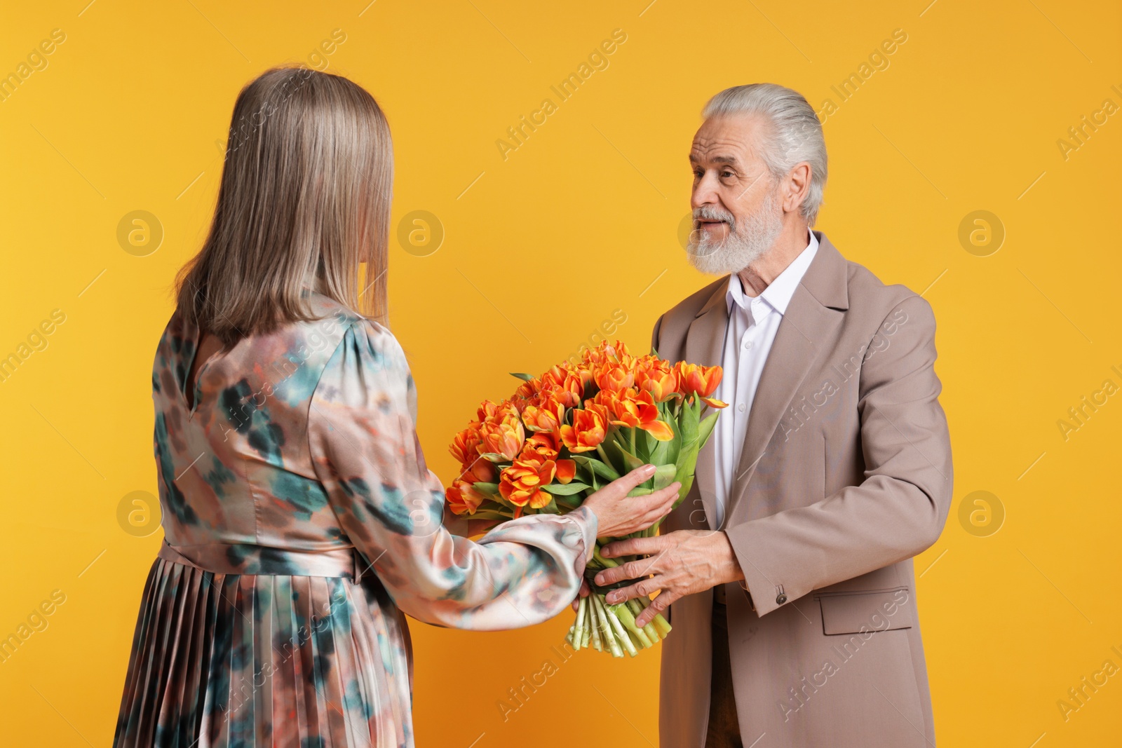 Photo of Man presenting bouquet of tulips to his wife on yellow background