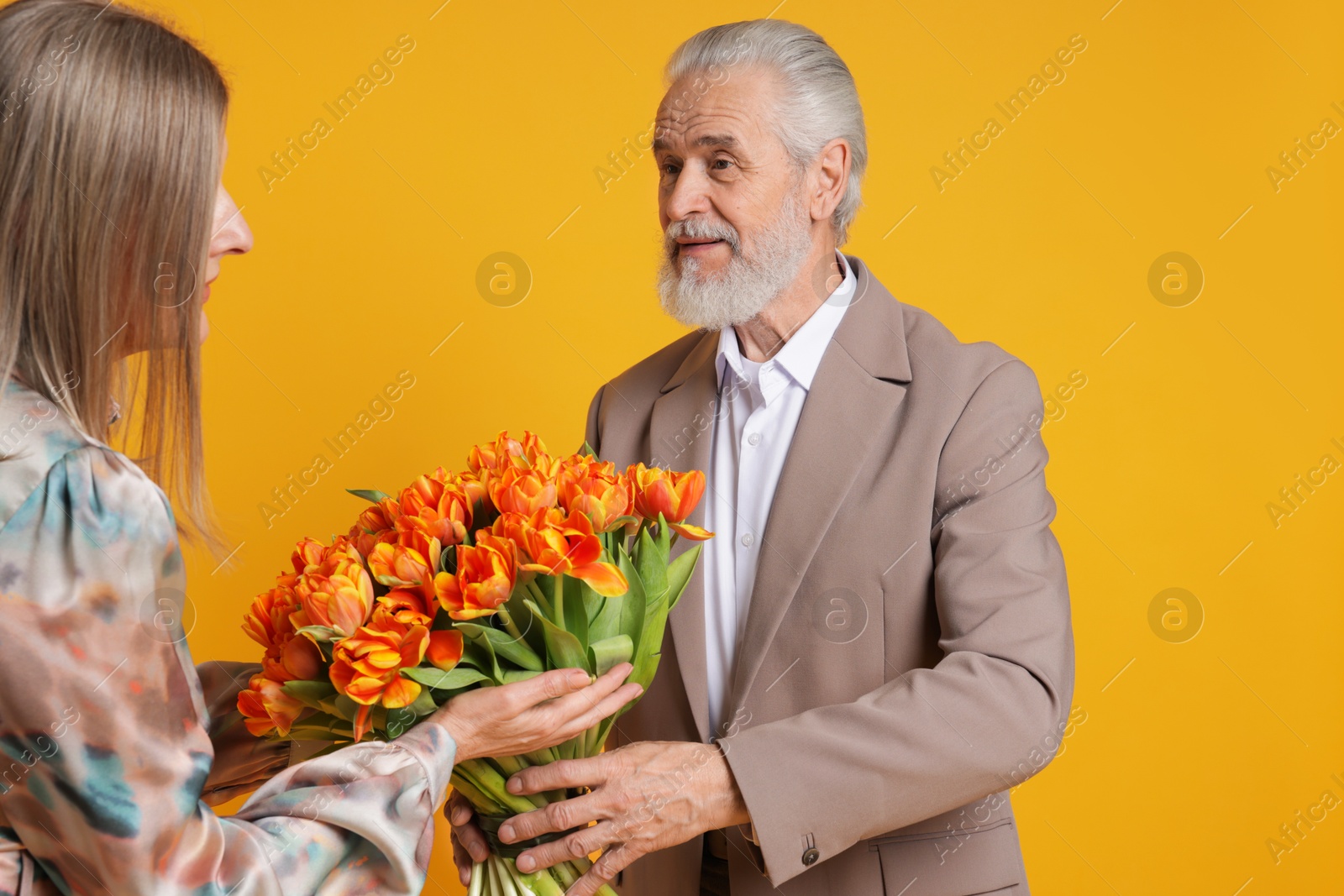 Photo of Man presenting bouquet of tulips to his wife on yellow background