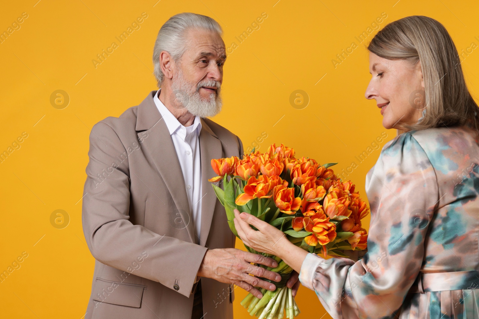 Photo of Man presenting bouquet of tulips to his happy wife on yellow background