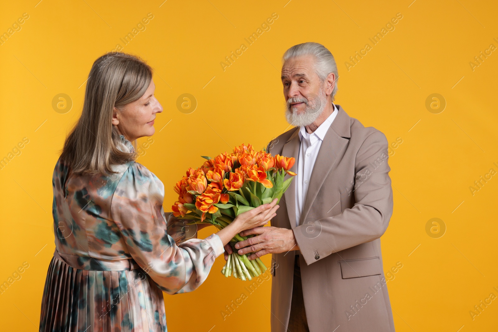 Photo of Man presenting bouquet of tulips to his wife on yellow background