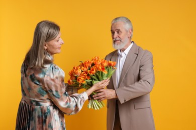 Photo of Man presenting bouquet of tulips to his wife on yellow background