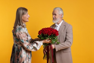 Photo of Cute couple with bouquet of red roses on yellow background