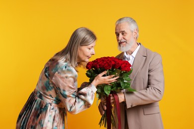 Photo of Cute couple with bouquet of red roses on yellow background